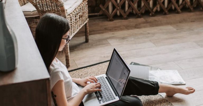 Loyalty Program - Young barefoot woman using laptop on floor near books in stylish living room