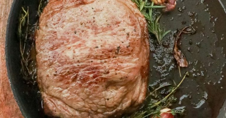 Steak Cuts - Top view of piece of meat steak in hot pan with rosemary and garlic placed on wooden cutting board in kitchen