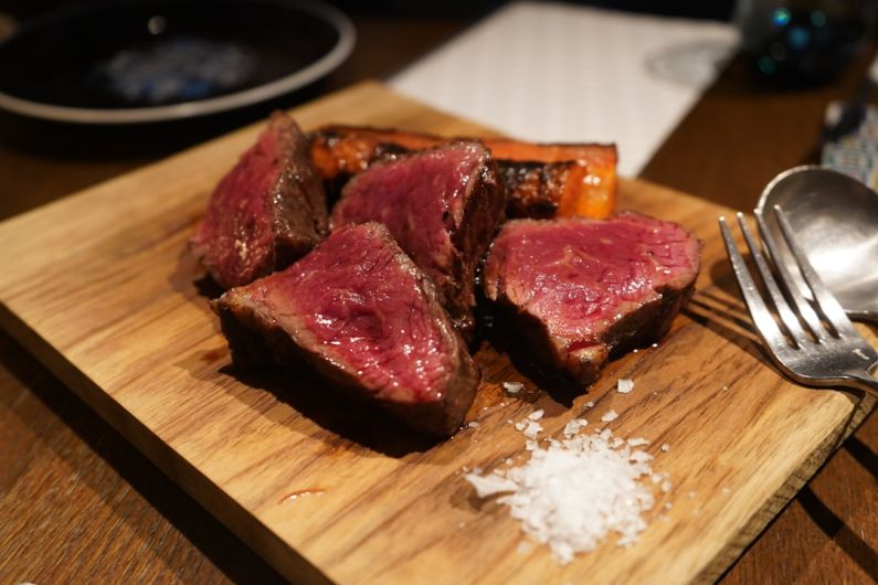 Steakhouses - a piece of meat on a cutting board with a fork and spoon